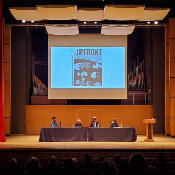 Panelists Martin Wannam, Lucy Lippard, Daniel Flores y Ascencio, and Abigail Satinsky seated at a table on a large stage.
