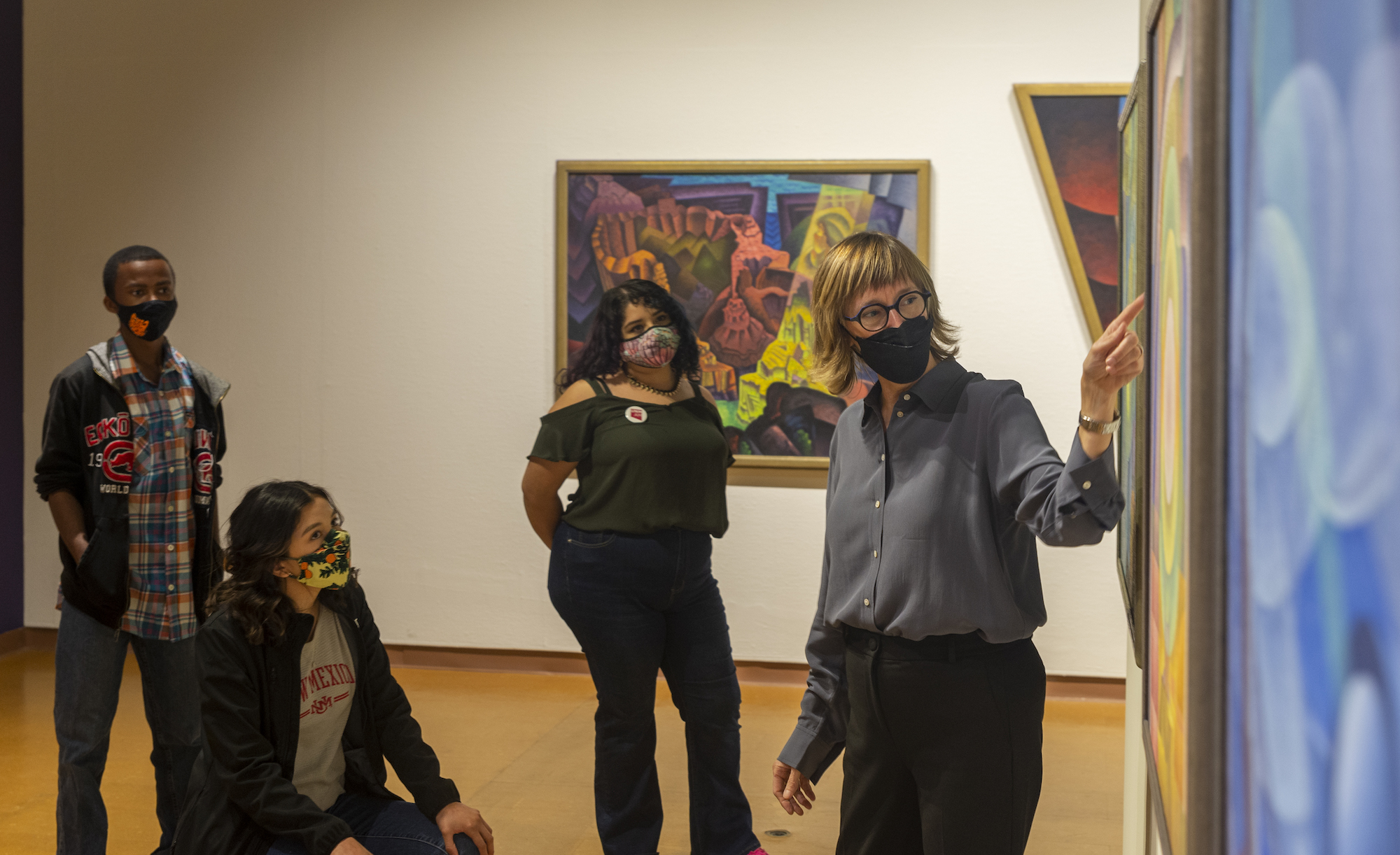 Curator Mary Statzer is photographed leading a gallery tour of "Visionary Modern: Raymond Jonson Trilogies, Cycles, and Portraits," with three college students in attendance.
